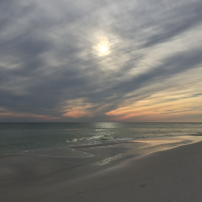 A hazy sun over a calm ocean shoreline at dusk